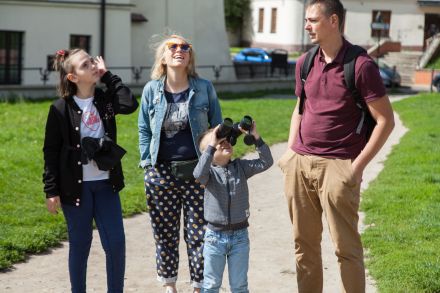 Rodzina uczestnicząca w spacerze. Chłopiec patrzy przez lornetkę w niebo.