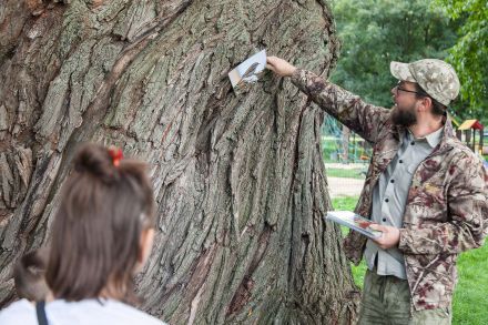 Przewodnik umieszcza zdjęcie ptaka na pniu drzewa. Widać dwoje dzieci, które mu się przyglądają.