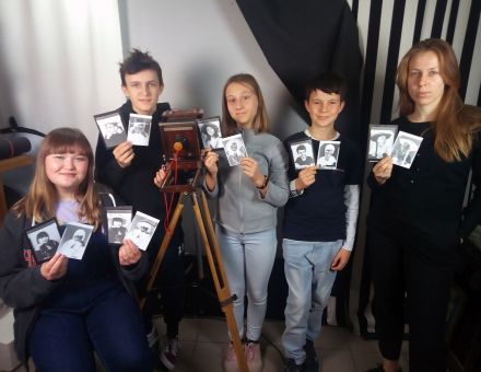 Grupa dzieci. Każdy trzyma w ręce dwa czarno-białe portrety.