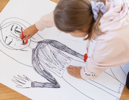 Dziewczynka maluje usta postaci, którą narysowała na kartce.