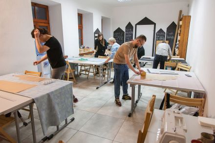 W pomieszczeniu przy stolikach każdy robi swoją kurtkę przeciwdeszczową.