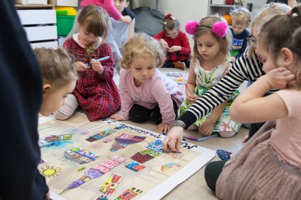 Dzieci siedzą przed plakatem i przyglądają mu się.