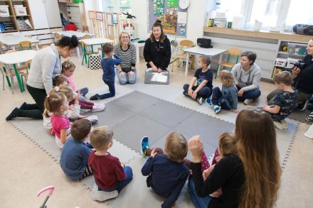 Dzieci siedzą w kręgu z prowadzącą zajęcia.