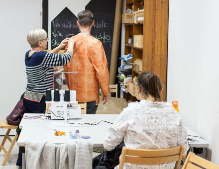 Kobieta robi pomiary na mężczyźnie i sprawdza, czy kurtka którą uszył, jest na niego dobra.