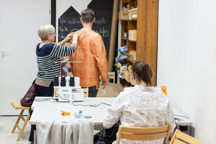 Kobieta robi pomiary na mężczyźnie i sprawdza, czy kurtka którą uszył, jest na niego dobra.