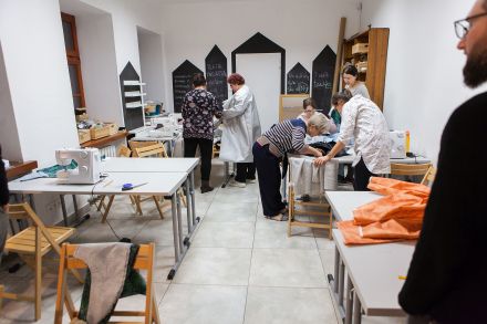 Na sali przy stolikach każdy szyje na maszynie swoją kurtkę przeciwdeszczową.