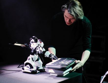 Mężczyzna trzyma instrument klawiszowy, na którym gra robot.