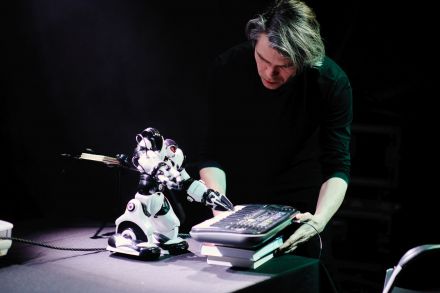 Mężczyzna trzyma instrument klawiszowy, na którym gra robot.