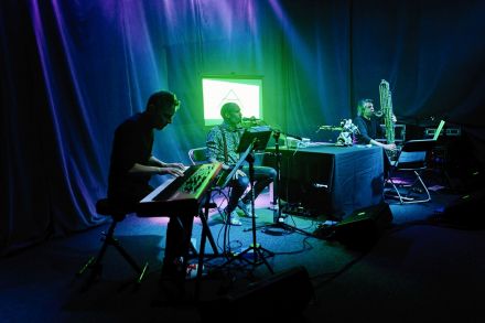 Scena sfotografowana z boku. Kolejno muzycy: keyboardzista, wokalista, robot i saksofonista.