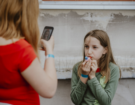 Kobieta robi zdjęcie dziewczynce, która gwiżdże na świeżo pomalowanym ptaszku.