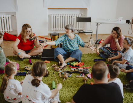 Uczestnicy warsztatów siedzą w okręgu. Na środku leżą instrumenty muzyczne.