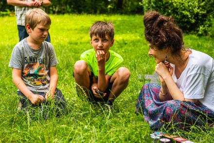Animatorka oraz dwaj chłopcy siedzą na trawie.