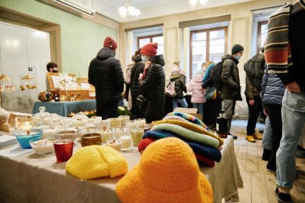 Ludzie chodzą między stoiskami. Widać stoisko ze świecami oraz czapkami wełnianymi.