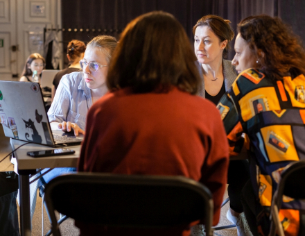Przy jednym stoiku siedzą cztery dziewczyny i sprawdzają coś w laptopie.