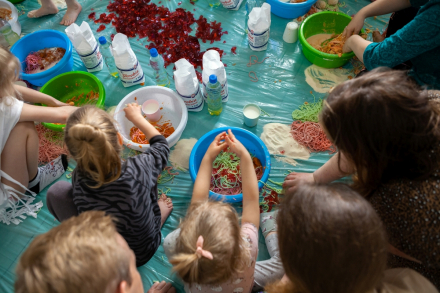 Dzieci siedzą na folii i rozłożonej na podłodze i mieszają w miskach różne produkty.