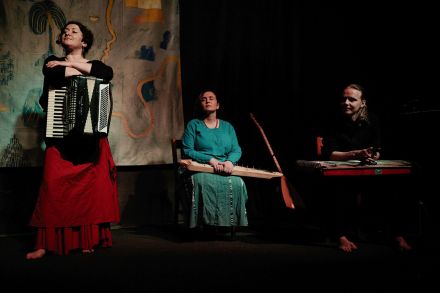 Zdjęcie trzech członków zespołu muzycznego trzymających instrumenty na scenie.