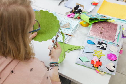 Kobieta wycina nożyczkami zielonego kwiatka, którego przyklei do  książeczki.