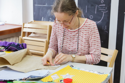Kobieta odrysowuje na materiale kształty, które chce przyszyć do książeczki.