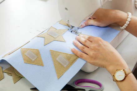 Kobieta zszywa kawałki materiałów na  maszynie. Widzimy tylko jej dłonie.