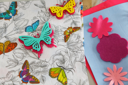 Do szarego materiału przyszyte są kolorowe motyle.