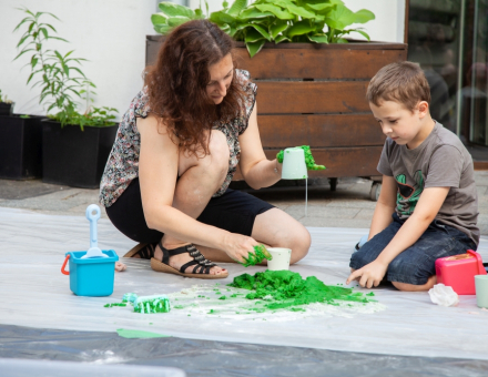 Chłopiec z animatorką wylewają na podłoże zieloną masę. Animatorka ma zabrudzone na zielono dłonie.