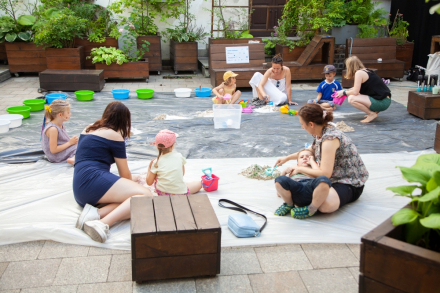 Wszyscy uczestnicy warsztatów podczas zabawy. Dzieci siedzą w grupach z animatorkami i bawią się piaskiem.