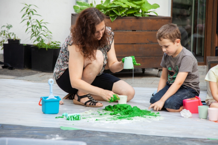 Chłopiec z animatorką wylewają na podłoże zieloną masę. Animatorka ma zabrudzone na zielono dłonie.