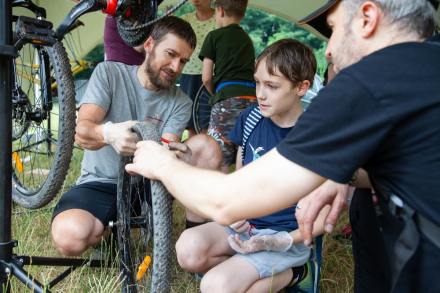 Dwaj mężczyźni trzymają koło od roweru. Chłopiec sprawdza czy jest napompowane.