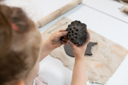 Dziewczynka trzyma w ręce gliniany dzwonek wietrzny.