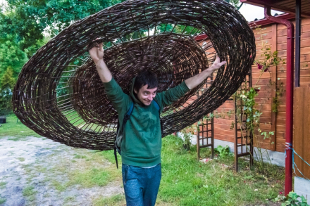 Mężczyzna niesie na plecach ogromne koło wyplecione z wikliny.