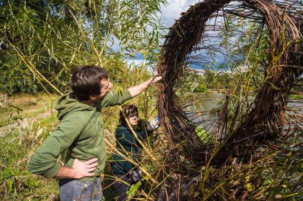 Mężczyzna wskazuje na okrąg z wikliny. W tle widać wodę.