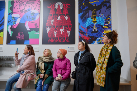 Uczestniczki wernisażu wystawy podsumowującej projekt "Trans-making" patrzą poza kadr. Jedna z kobiet, brunetka w łososiowym płaszczu nagrywa telefonem coś, co ma miejsce poza kadrem