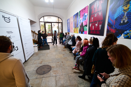 Rzut ogólny na dużą grupę osób znajdujących się na korytarzu Warsztatów Kultury. Słuchają dwóch kobiet opowiadających o wystawie i projekcie Trans-making