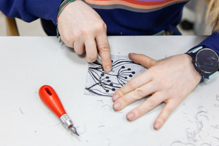 Dłonie dziecka, które siedzi przy stole i robi linoryt.