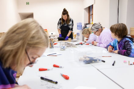 Uczestnicy warsztatu siedzą przy stole i robią linoryt,