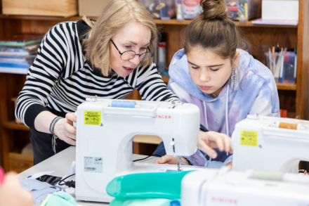 Animatorka pokazuje dziewczynie jak obsługuje się maszynę do szycia.