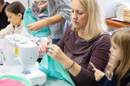 Grupa kobiet siedzi przy stole i zszywa kawałki materiałów.