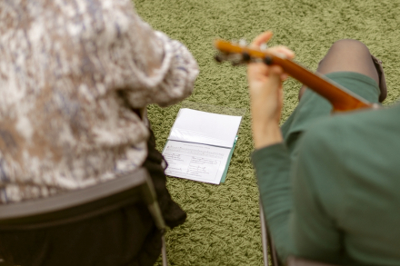 Dwie kobiety siedzące tyłem. Na dywanie przed nimi leży zeszyt z nutami.