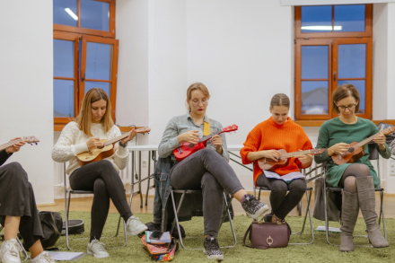 Cztery kobiety biorące udział w warsztacie siedzą na krzesłach i grają na ukulele.