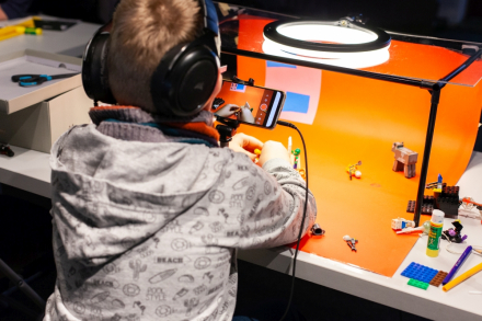 Chłopiec ma na głowie słuchawki. Siedzi przy stoliku z telefonem w ręce i robi zdjęcia.