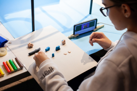 Chłopiec buduje coś z klocków lego na stoliku. Obok leży telefon komórkowy.