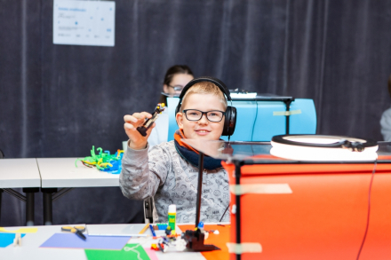 Dziewczynka w słuchawkach na głowie uśmiecha się do obiektywu.