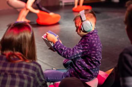 Chłopiec siedzi ze słuchawkami wyciszającymi na głowie. Ogląda książkę.