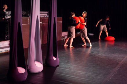 Trzy kobiety-aktorki biją się na scenie poduszkami. Obok wiszą również trzy kokony.