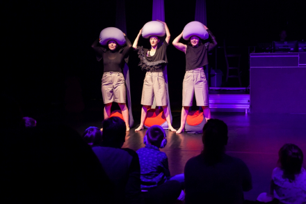 Trzy aktorki na scenie z poduszkami na głowach.