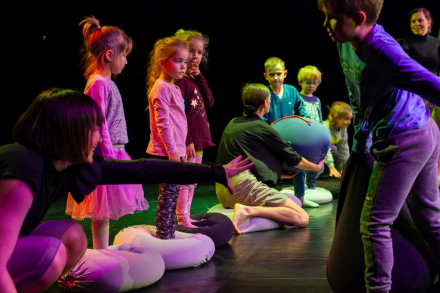 Dzieci i rodzice na scenie stoją w rzędzie. Każde dziecko ma swoją poduszkę.