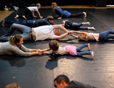 Rodzice z dziećmi leżą na podłodze i trzymają się za ręce.