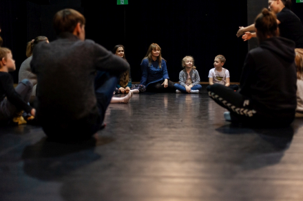 Rodzice z dziećmi siedzą w okręgu na podłodze.