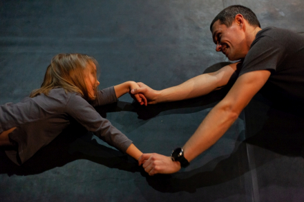 Dziewczynka z tatą leżą na podłodze i trzymają się rękami.