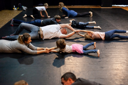 Rodzice z dziećmi leżą na podłodze i trzymają się za ręce.